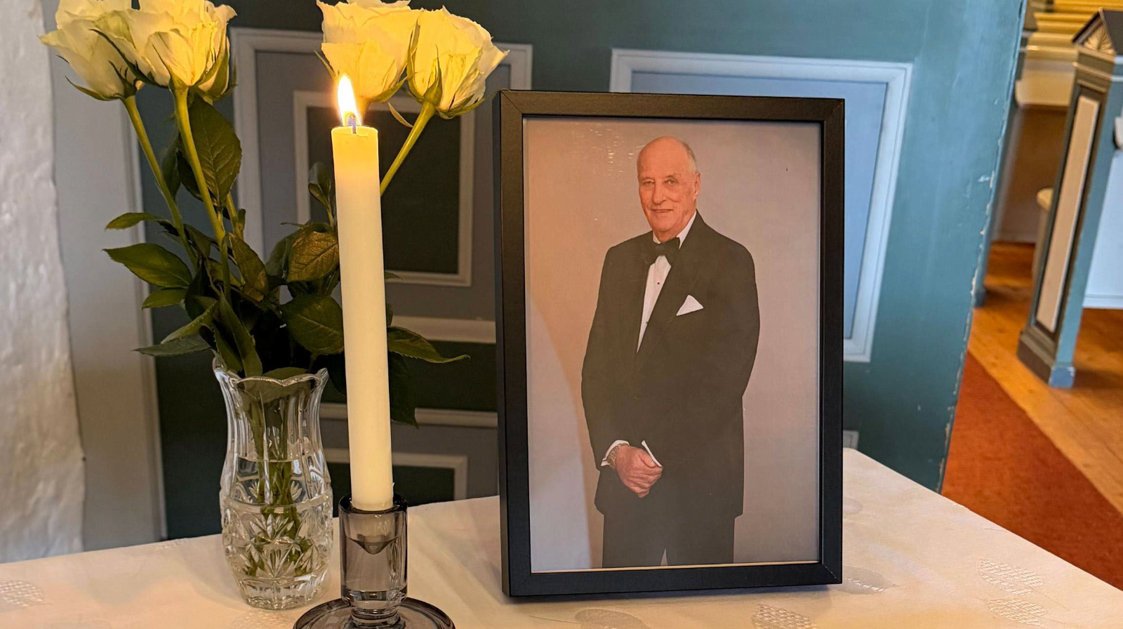 Bord med bilde av H.M. Kong Harald, levende lys, blomster og kondolanseprotokoll.